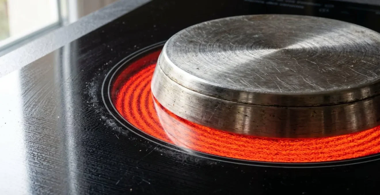 Gros plan sur une surface de plaque à induction noire avec zone de cuisson activée et casserole en acier inoxydable